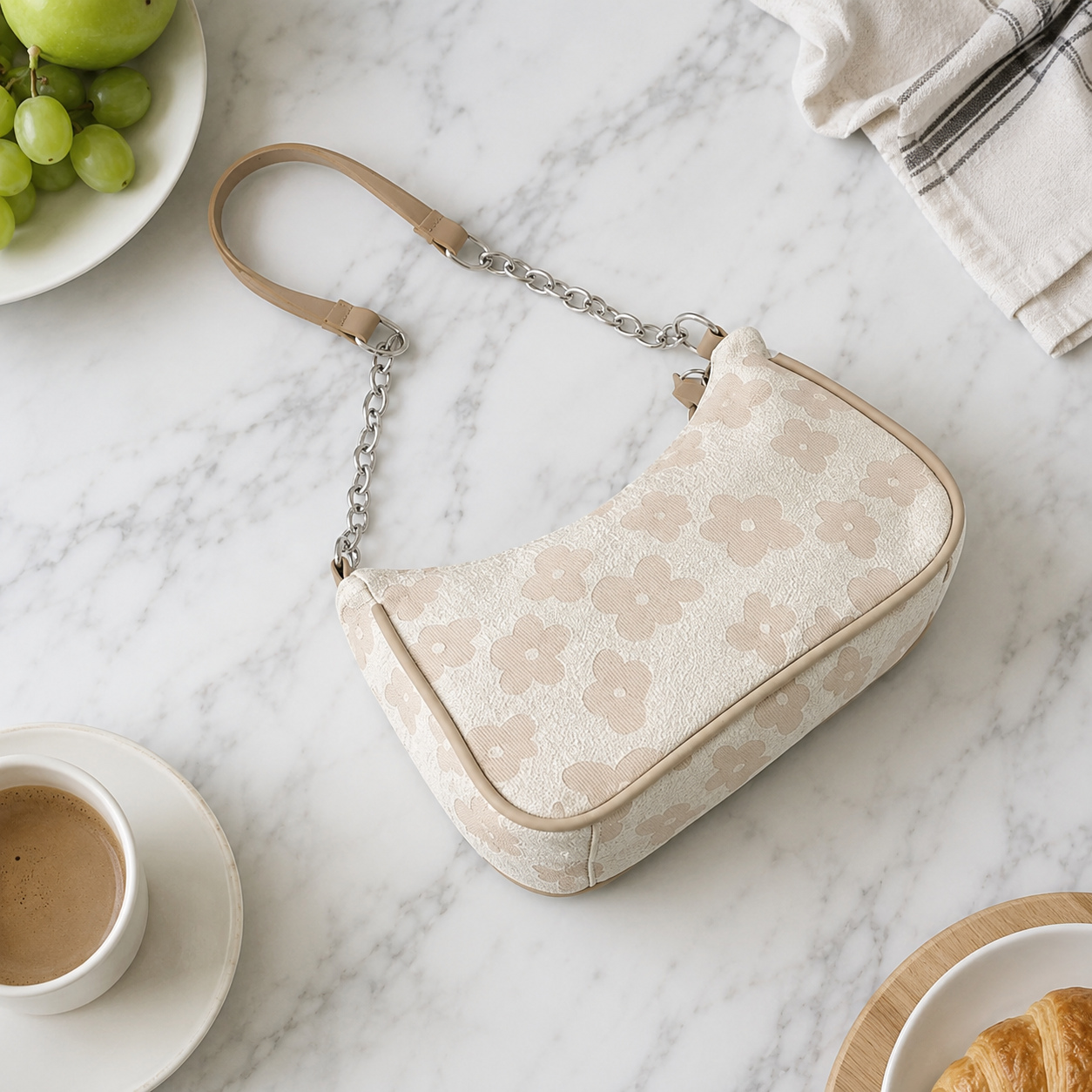 Arivon cream floral-pattern shoulder bag on white marble beside a cup of coffee, grapes, and a croissant